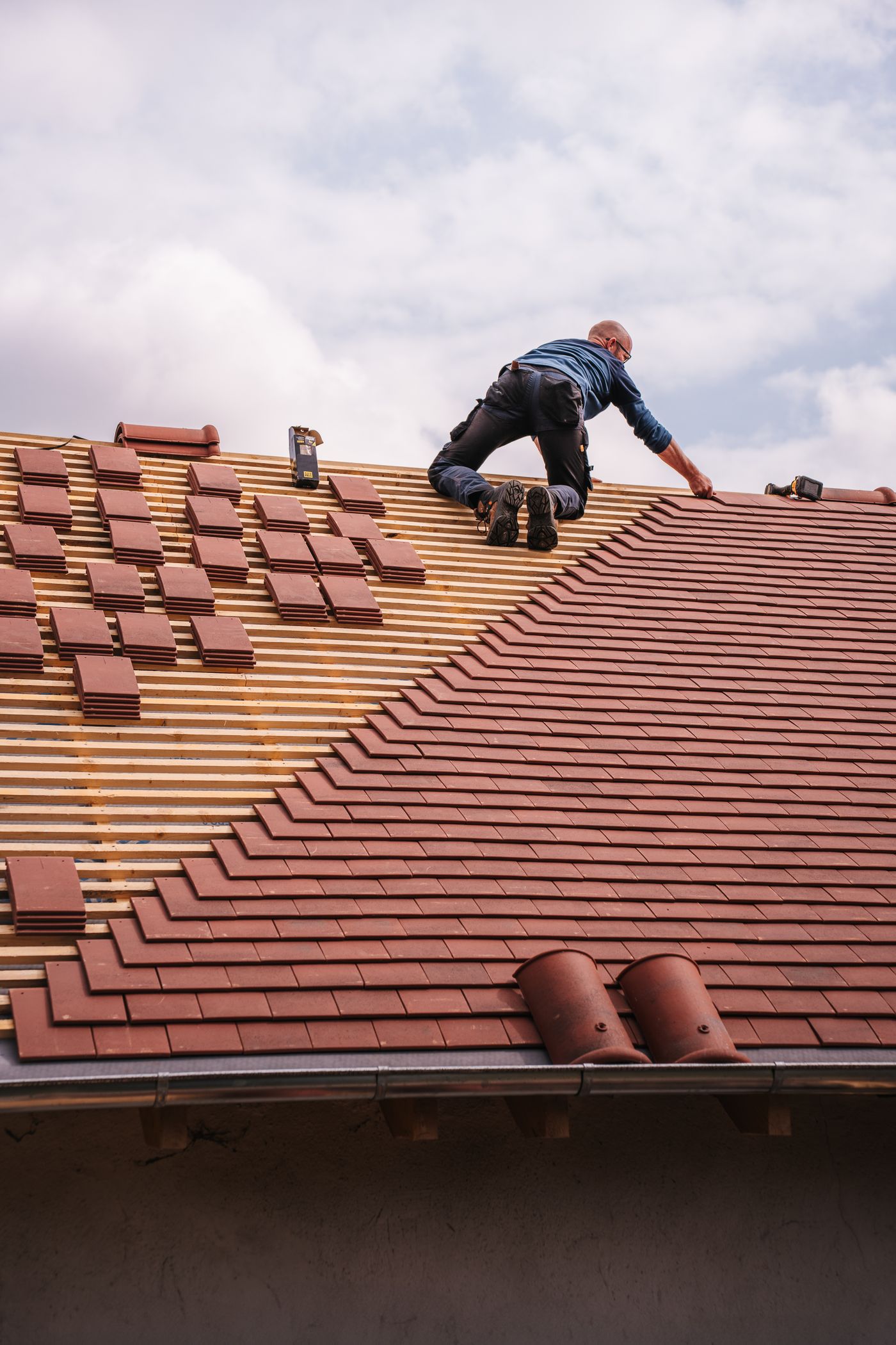 Dachdecker verlegt rote Tonziegel auf der Dachlattung eines Steildachs.